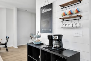 A modern kitchen with a coffee maker, a chalkboard sign, and mugs on shelves.