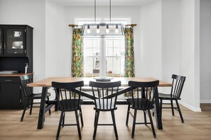 A dining area with a wooden table and black chairs, a black cabinet with glass doors, and a window with curtains. - Walk to Oak Island Beach! Casablanca Estate (Oak Island)