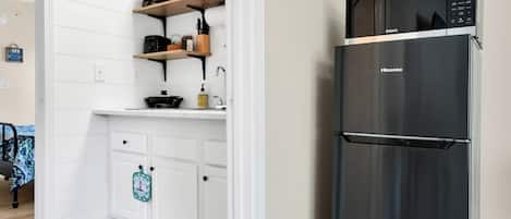 Una cocina con muebles blancos, un refrigerador de acero inoxidable y un estante de madera con utensilios de cocina.