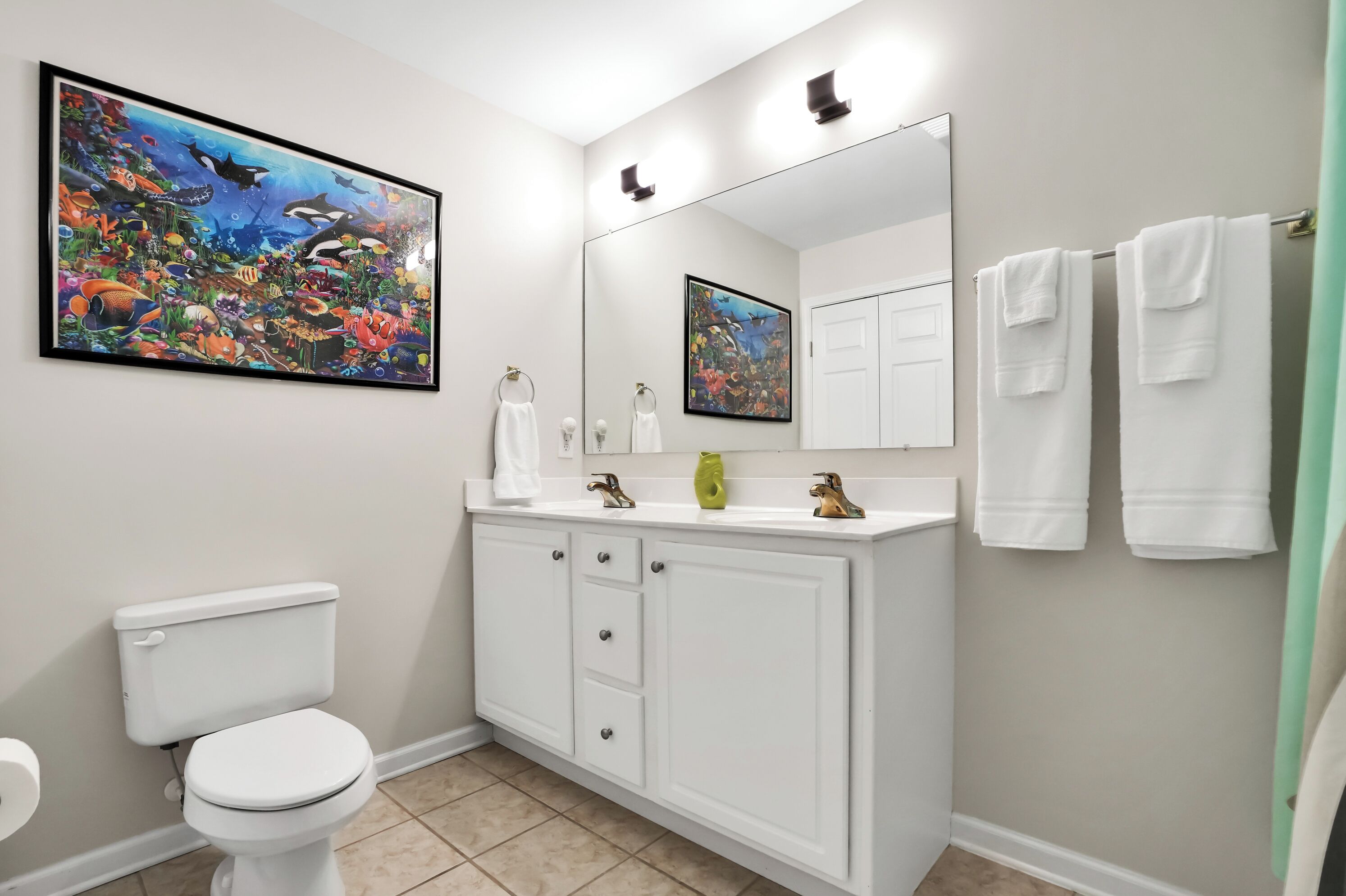 Een badkamer met toilet, een witte wastafel, een spiegel en een grote wanddecoratie van een vis.