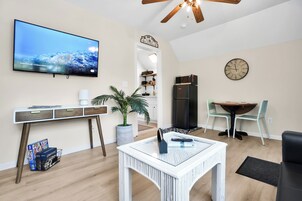 Una sala moderna con televisor de pantalla plana, un comedor con mesa y sillas, una cocina con refrigerador y un ventilador de techo.