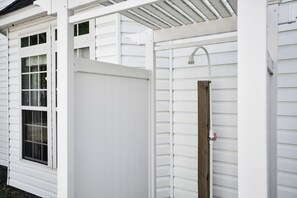 A white exterior with a wooden door, a window, and a metal showerhead. - Walk to Oak Island Beach! Casablanca Estate (Oak Island)