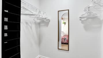 A hallway with a mirror, a black shelving unit, and a bed with a patterned bedspread.