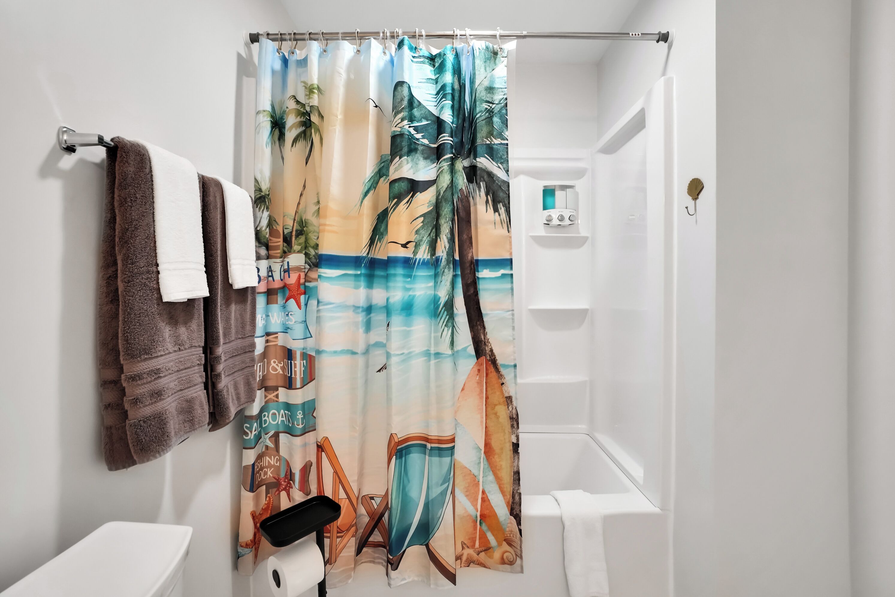 A bathroom with a shower curtain depicting a beach scene, a toilet, and a towel rack with two towels.