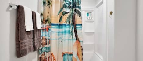 Un baño con cortina de ducha decorada con una escena de playa, un inodoro y un perchero con dos toallas.