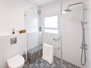 Ein Badezimmer mit Duschkabine, Toilette, Handtuchhalter und Fenster.