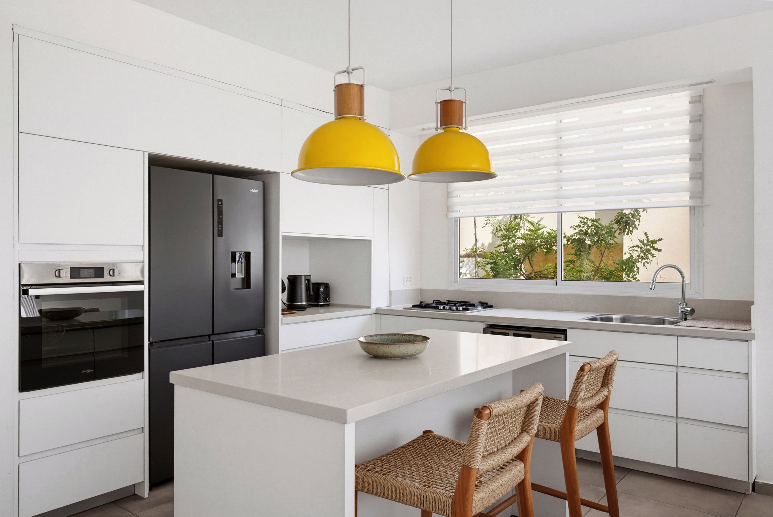 A modern kitchen with a central island, stainless steel appliances, and a window with blinds.