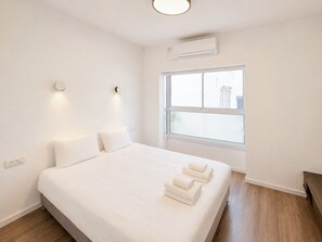 Ein schlichter Schlafzimmer mit einem großen Bett, einem Fenster mit Aussicht und einer Klimaanlage.