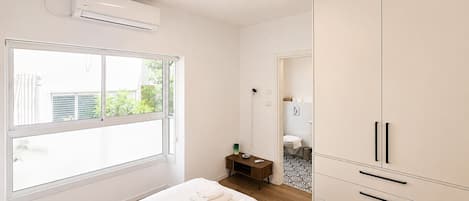 A bedroom with a large window, a bed with neatly folded towels, a wardrobe, and an air conditioning unit.