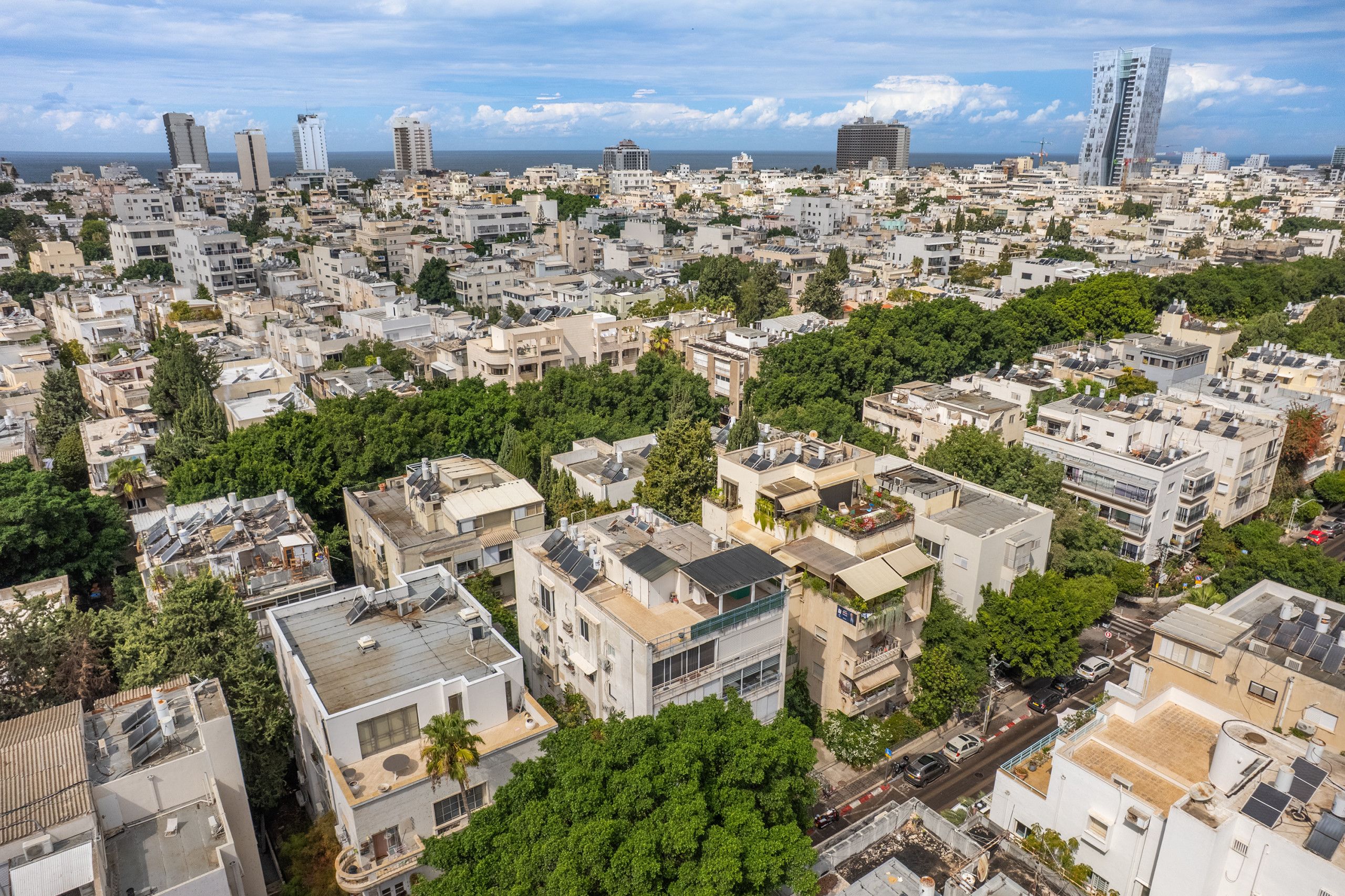 Ein dicht bebautes Stadtgebiet mit zahlreichen Gebäuden, von denen einige mit sichtbaren Solaranlagen auf den Dächern ausgestattet sind, und im Hintergrund ein klarer Blick auf das Meer.