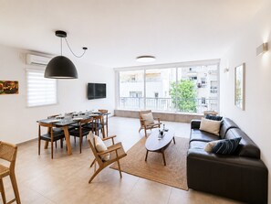 Ein modernes Wohnzimmer mit Essbereich, großen Fenstern und einem schwarzen Ledersofa.