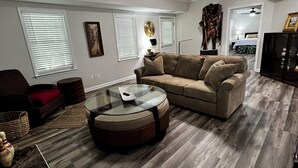 A living room with a sectional sofa, a glass coffee table, a ceiling fan, and a view into the bedroom. - Spacious 1-bedroom apartment in brilliant Peachtree City (PEACHTREE CITY)