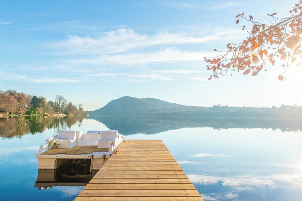 A wooden dock extending into calm water with a boat docked at the end. - Villa Evelina (Travedona-Monate)