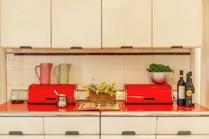 A kitchen with a red countertop, a red appliance, a metal pitcher, a bowl of green herbs, and two bottles of wine. - Villa Evelina (Travedona-Monate)