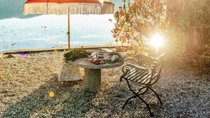 Eine Bank und ein Tisch mit Sonnenschirm mit Blick auf ein Gewässer.