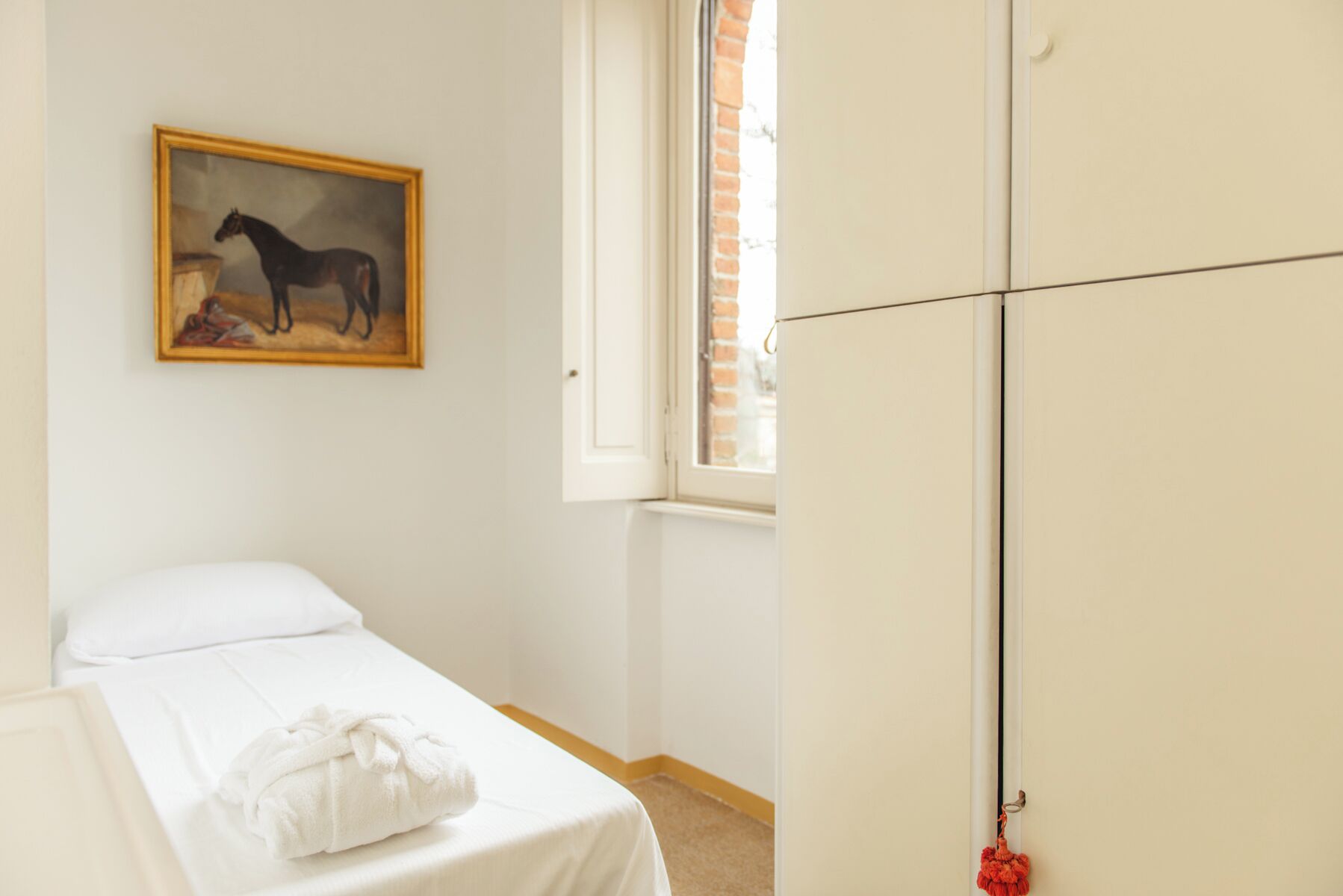 Una camera da letto con un letto, una parete bianca, un quadro raffigurante un cavallo e un armadio.