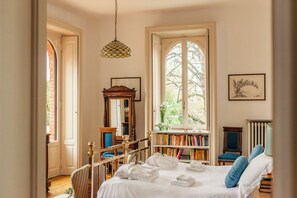 Een slaapkamer met een groot raam, een boekenkast, een radiator en een bed met handdoeken.