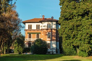 A two-story building with a brick facade, a balcony, and a well-maintained lawn. - Villa Evelina (Travedona-Monate)