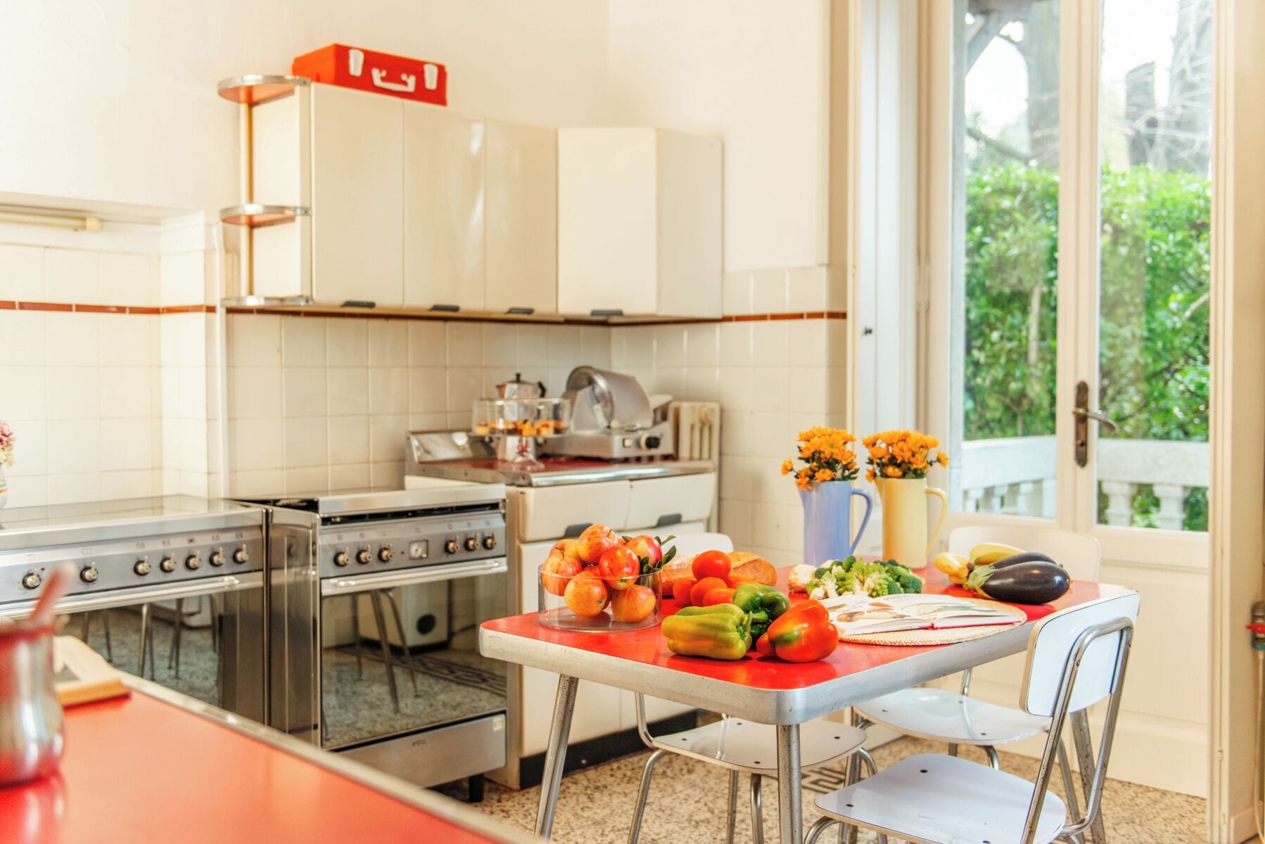 Una cucina con piano cottura, forno e mobili, un tavolo da pranzo con verdure, e una finestra vista verde.