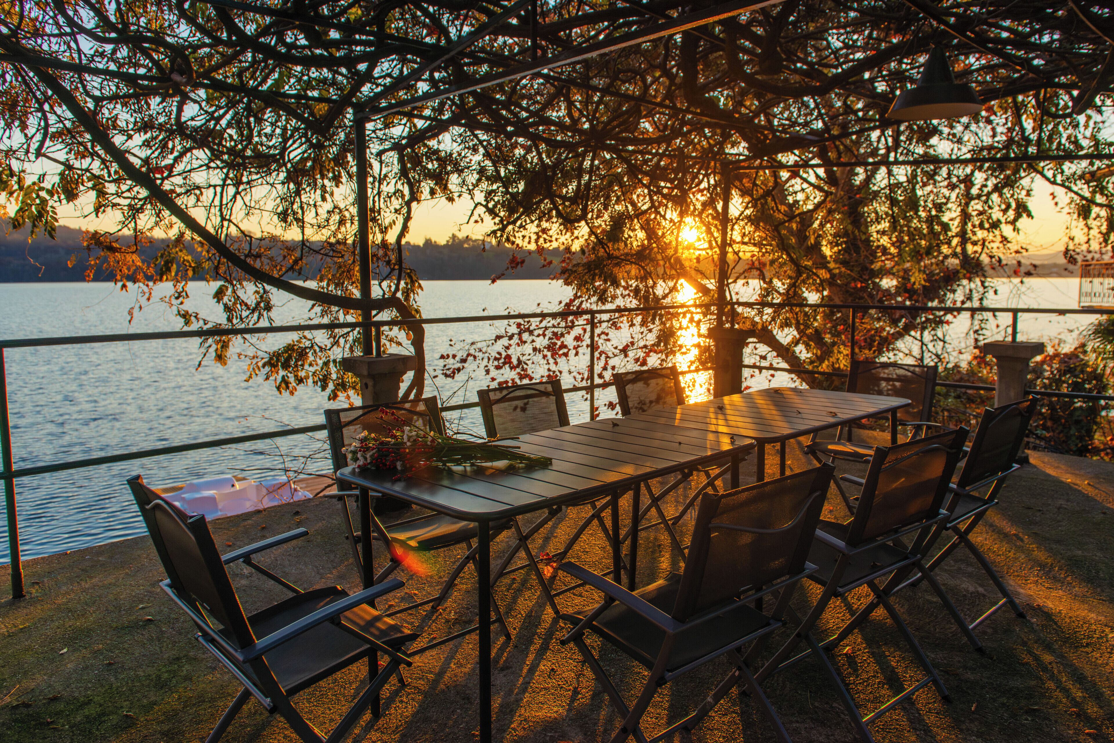 An outdoor dining area with a table and chairs, overlooking a body of water.