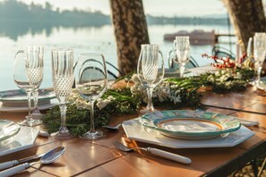 A table set for a meal with clear glassware, plates, and cutlery, overlooking a body of water. - Villa Evelina (Travedona-Monate)