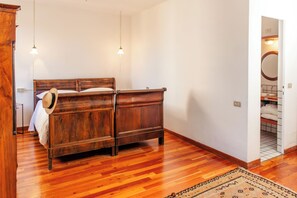 A bedroom with a wooden bed, two pendant lights, a patterned rug, and a view into the bathroom. - Villa La Limonera (Casciago)