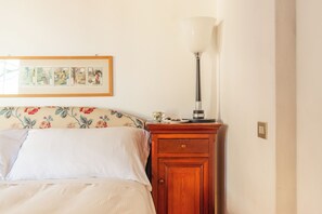 A bedroom with a bed, a wooden nightstand, a lamp, and a framed picture on the wall. - Villa La Limonera (Casciago)