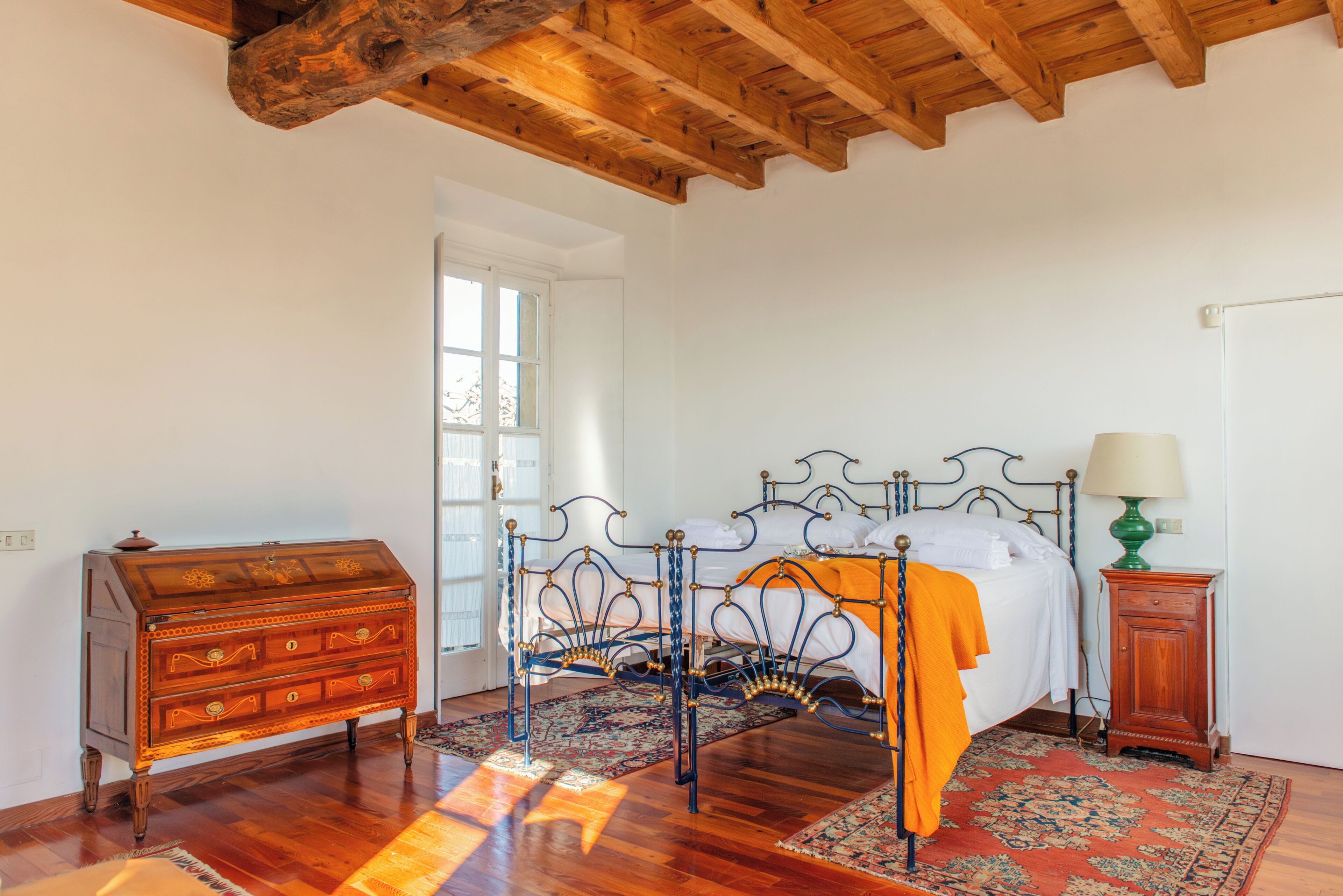 Un dormitorio con un aparador de madera, estructura de cama metálica, alfombra estampada y un armario de madera.