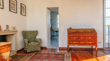 A room with a wooden dresser, a green floral armchair, a patterned rug, and framed pictures on the wall.