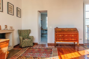 A room with a wooden dresser, a green floral armchair, a patterned rug, and framed pictures on the wall. - Villa La Limonera (Casciago)