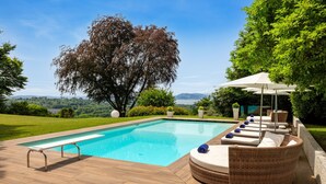 Ein Swimmingpool mit Liegestühlen und einer Pergola, umgeben von Grün und mit Blick auf die Landschaft.
