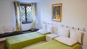 Ein Zimmer mit zwei Betten, einem Fenster mit Aussicht, einem Heizkörper und einem gerahmten Bild an der Wand.