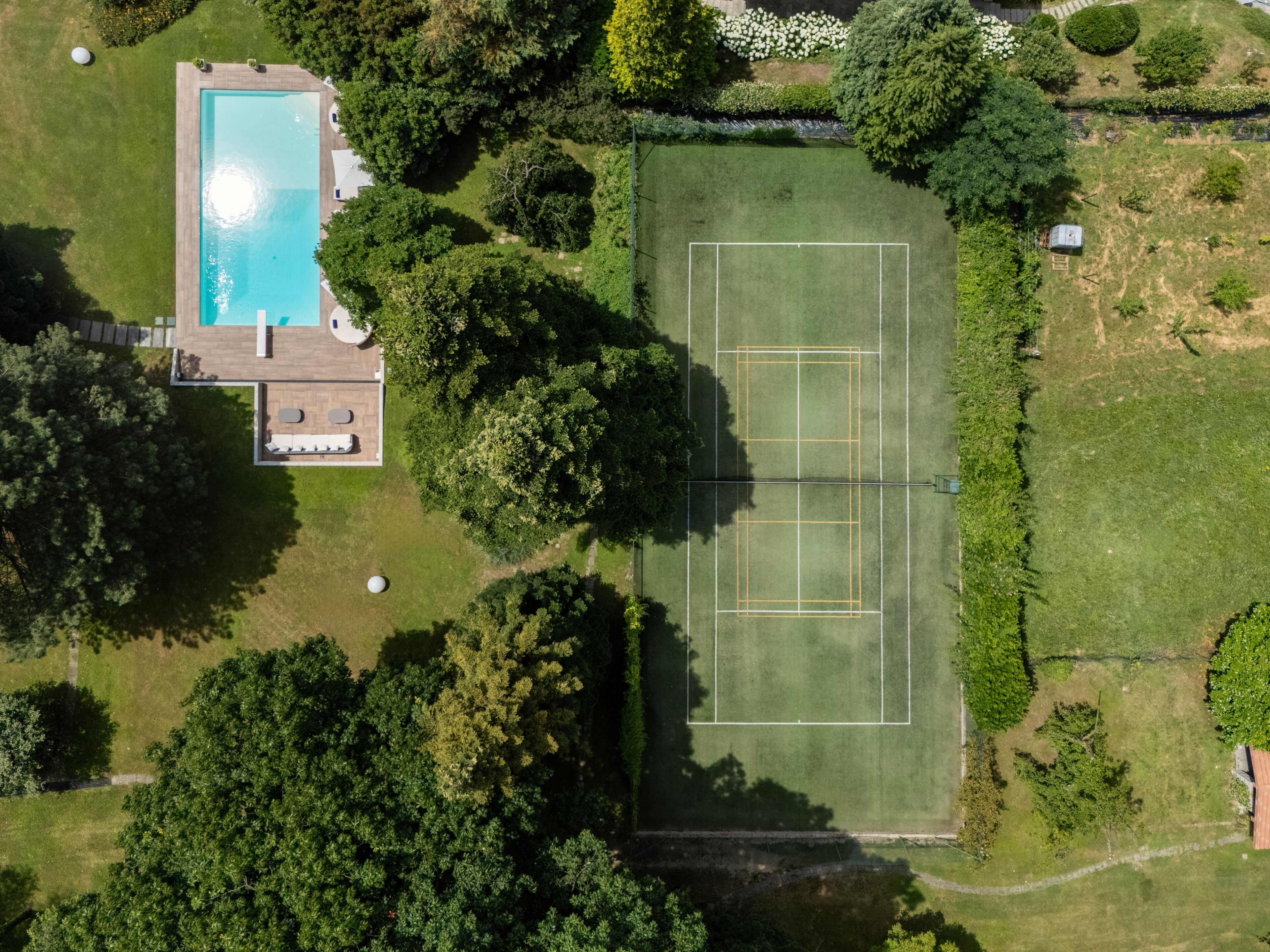 Vista aérea de una propiedad con piscina, cancha de tenis y abundante vegetación.