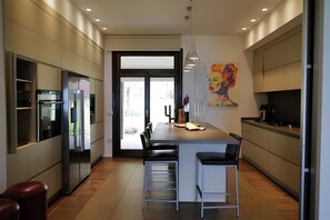 A modern kitchen with a central island, bar stools, and a large window. - Villa Serenity (Besozzo)