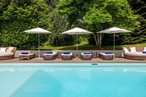 A poolside area with lounge chairs and umbrellas, surrounded by greenery. - Villa Serenity (Besozzo)