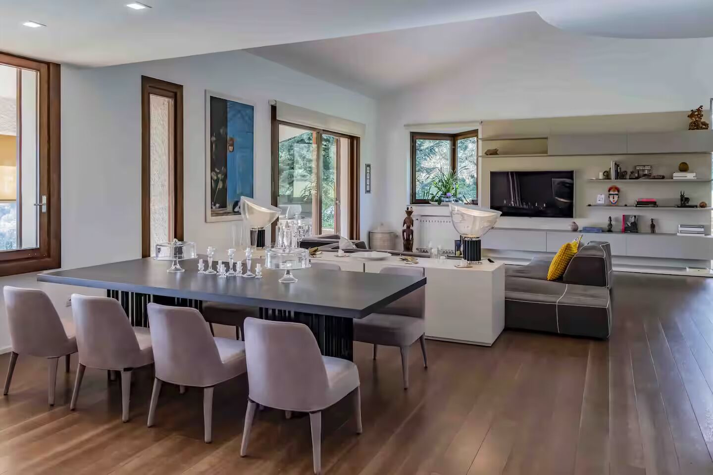 Una cucina moderna con una grande isola, una zona pranzo con un tavolo lungo e sedie, e un soggiorno con divano e televisore.