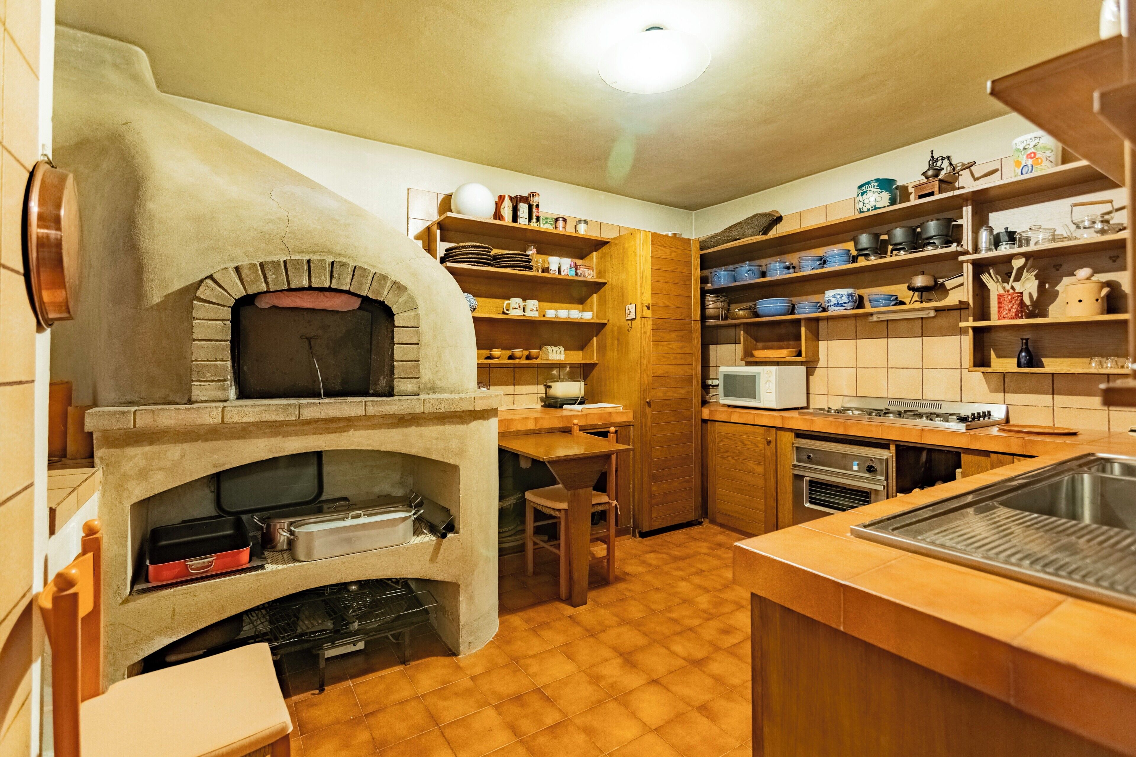 A kitchen with a built-in oven, wooden shelves, a microwave, and a sink.