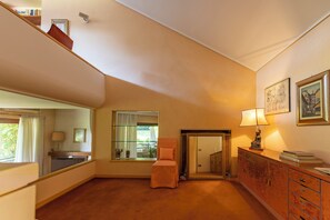 A room with a large mirror, a window with curtains, a chair, a cabinet with books, and a lamp. - Villa La Fortezza (Dormelletto)