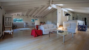 A spacious loft with a high ceiling, a white sofa, a red table, and a glass coffee table. - Villa La Fortezza (Dormelletto)