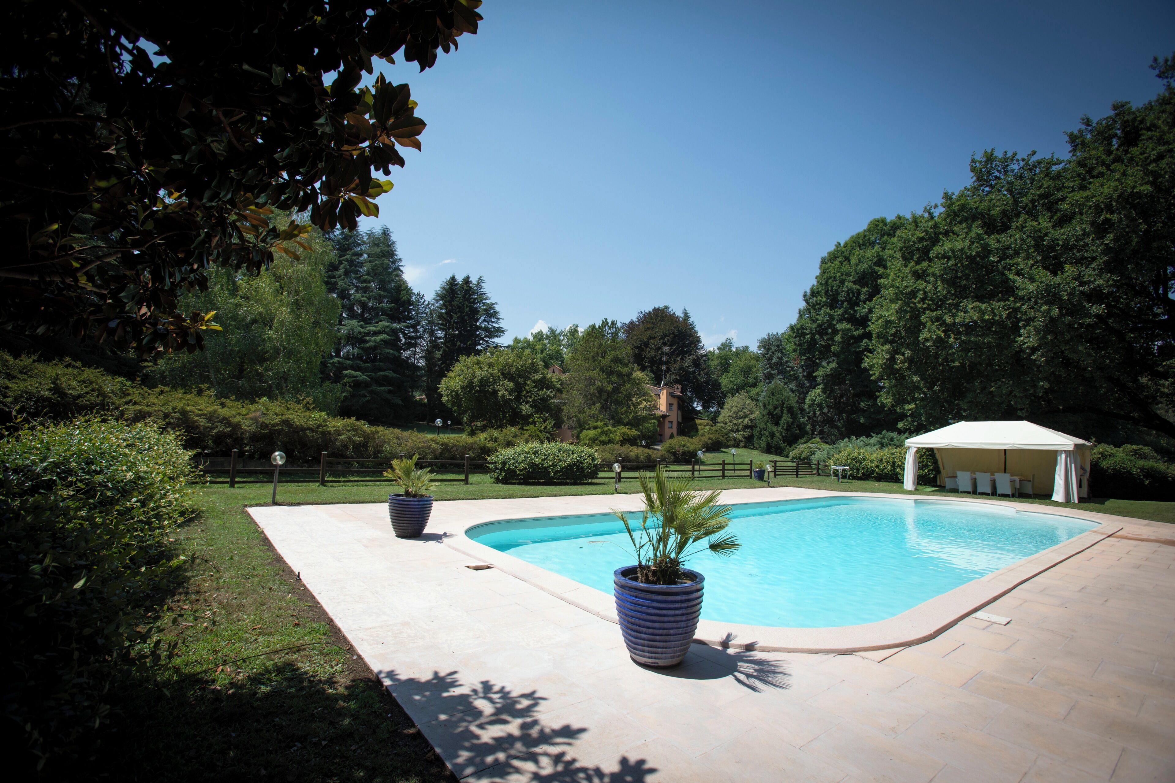 A swimming pool with a white canopy, surrounded by greenery and a paved deck.