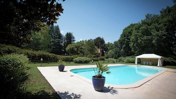 A swimming pool with a white canopy, surrounded by greenery and a paved deck.