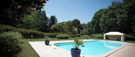 A swimming pool with a white canopy, surrounded by greenery and a paved deck.