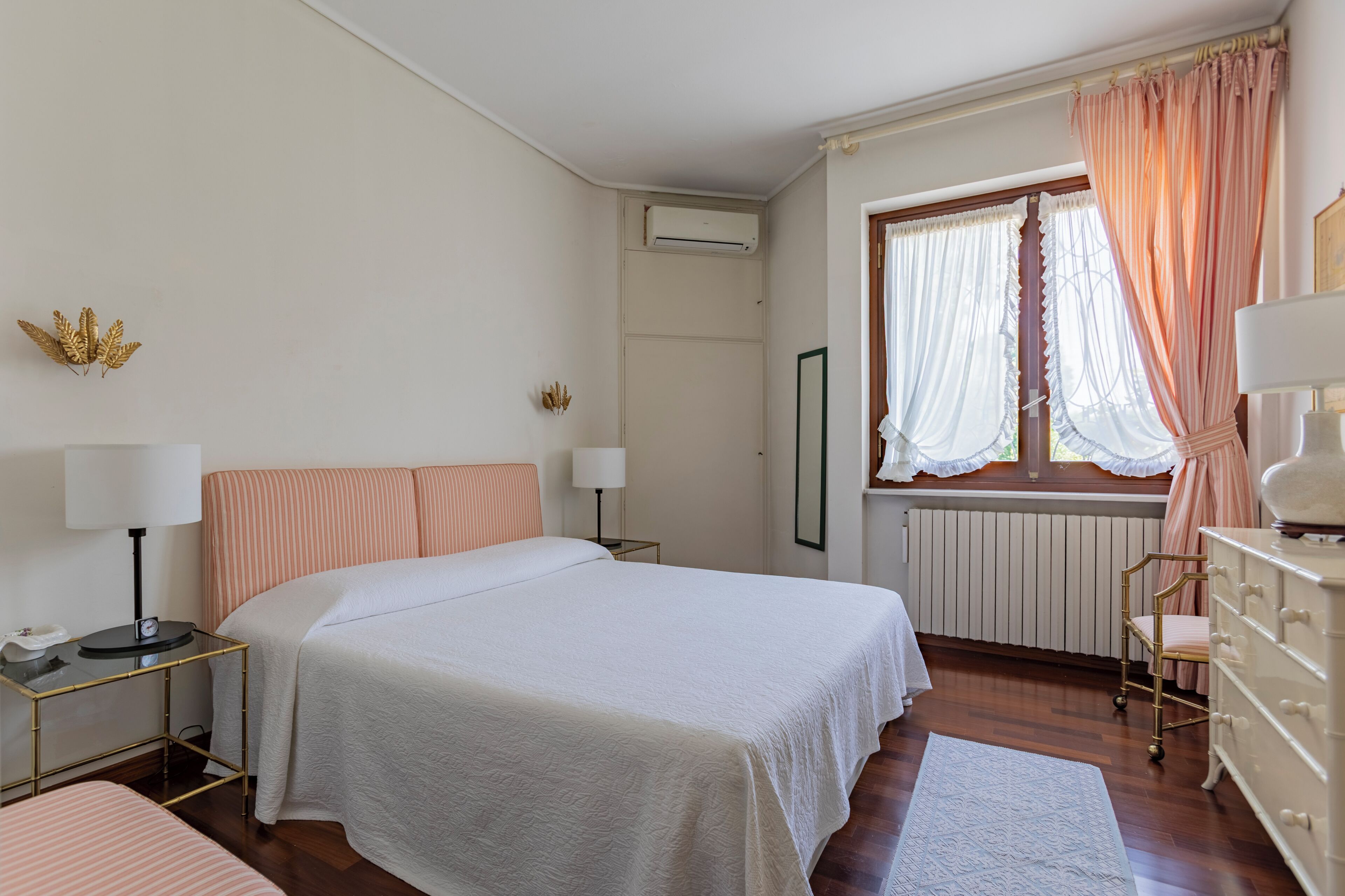 Une chambre à coucher comprenant un lit, des tables de chevet, une commode, une fenêtre avec des rideaux et un appareil de climatisation.