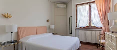 Une chambre à coucher comprenant un lit, des tables de chevet, une commode, une fenêtre avec des rideaux et un appareil de climatisation.