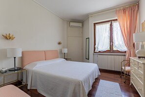 A bedroom with a bed, bedside tables, a dresser, a window with curtains, and an air conditioning unit.