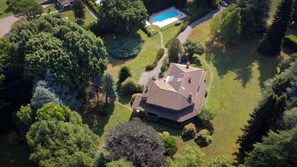 An aerial view of a residential property with a swimming pool, surrounded by lush greenery and a well-maintained lawn.