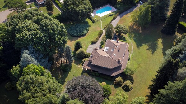 An aerial view of a residential property with a swimming pool, surrounded by lush greenery and a well-maintained lawn. - Villa La Fortezza (Dormelletto)