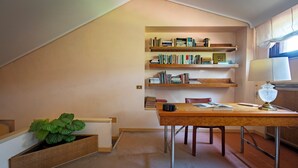 A study with a desk, bookshelf, lamp, and a potted plant. - Villa La Fortezza (Dormelletto)