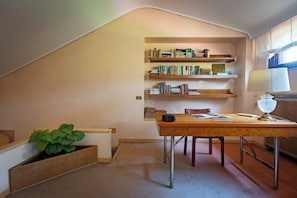 A study with a desk, bookshelf, lamp, and a potted plant.