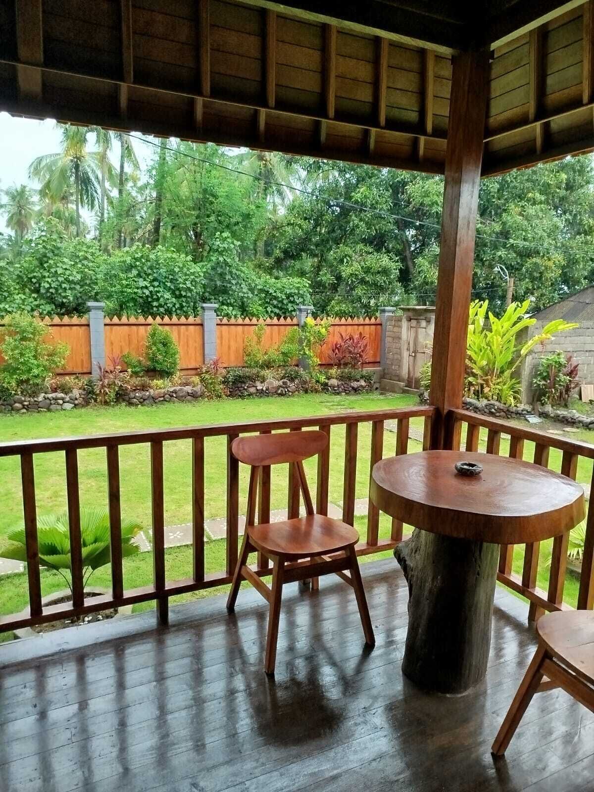 A wooden deck with a round table and two chairs, overlooking a garden with a wooden fence and various plants.